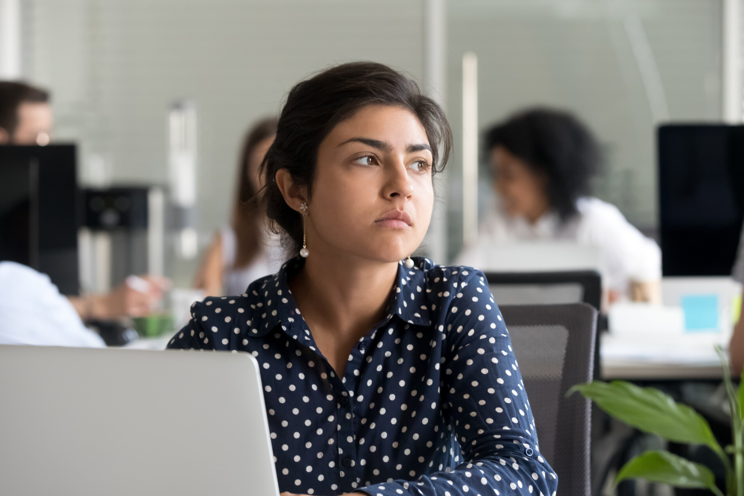 Young business woman sitting in front of her laptop in an office looking off into the distance